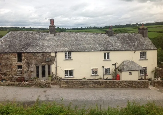 The granite exterior of Callisham Farm on a bright morning, with a garden gate and stone walls